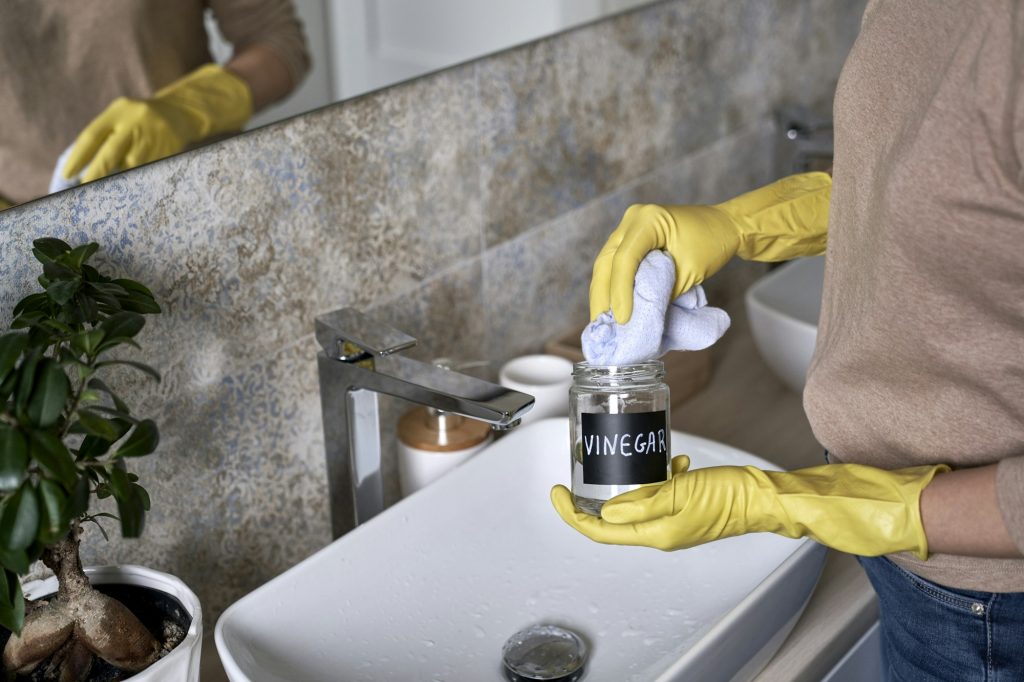 Unrecognizable woman cleaning bathroom tap with vinegar